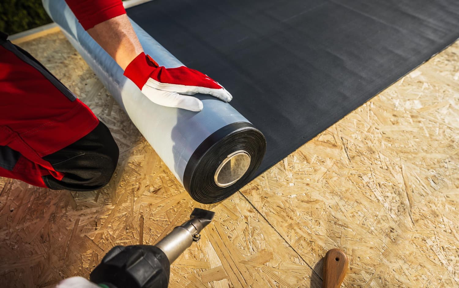 Dakwerker rolt EPDM-membraan uit op een nieuw plat dak met houten dakbeschot